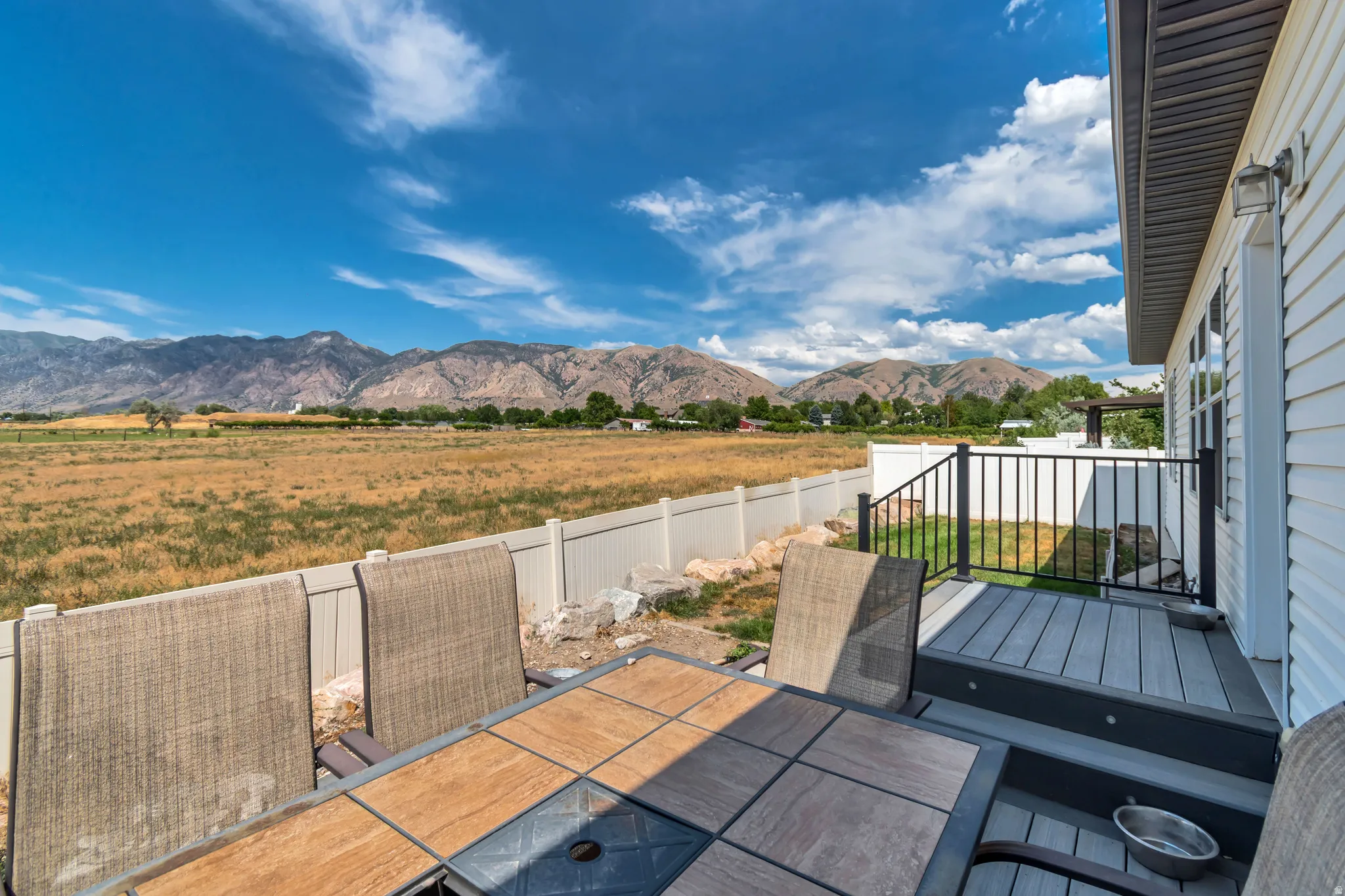Expansive outdoor living area featuring a multi-level deck with composite decking and black metal railings, a white vinyl fence, and a backdrop of distant mountains
