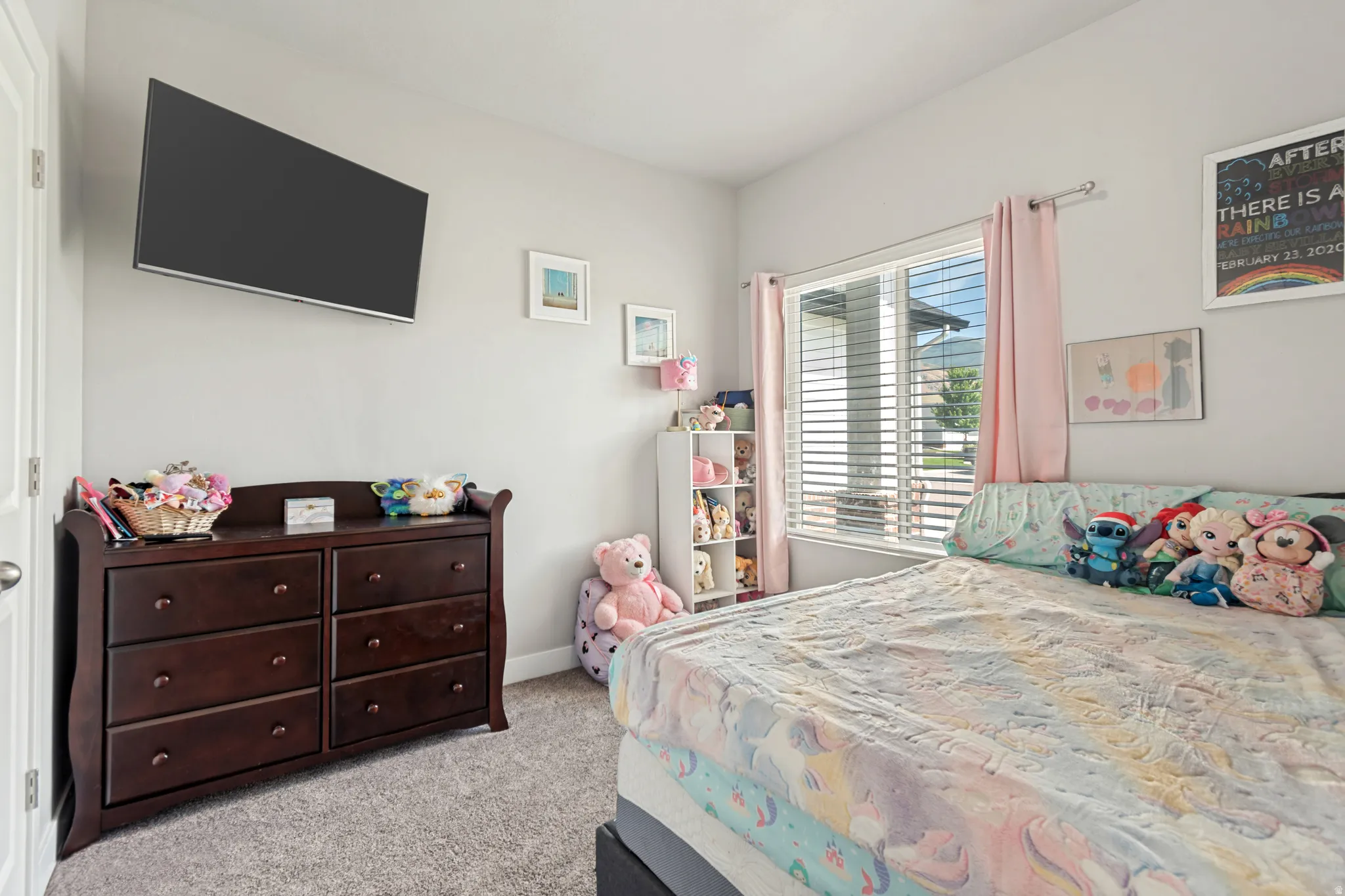 Carpeted bedroom featuring neutral wall paint, a wall-mounted television, and a window with blinds