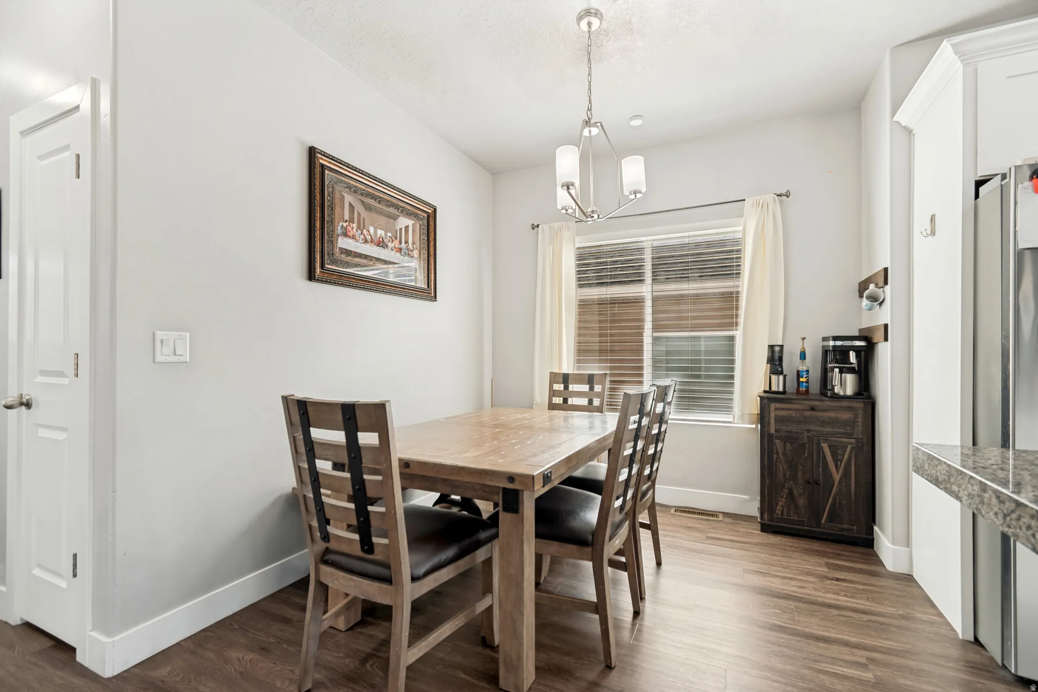 Dining area featuring wood-finish flooring, a contemporary chandelier, and a window with blinds