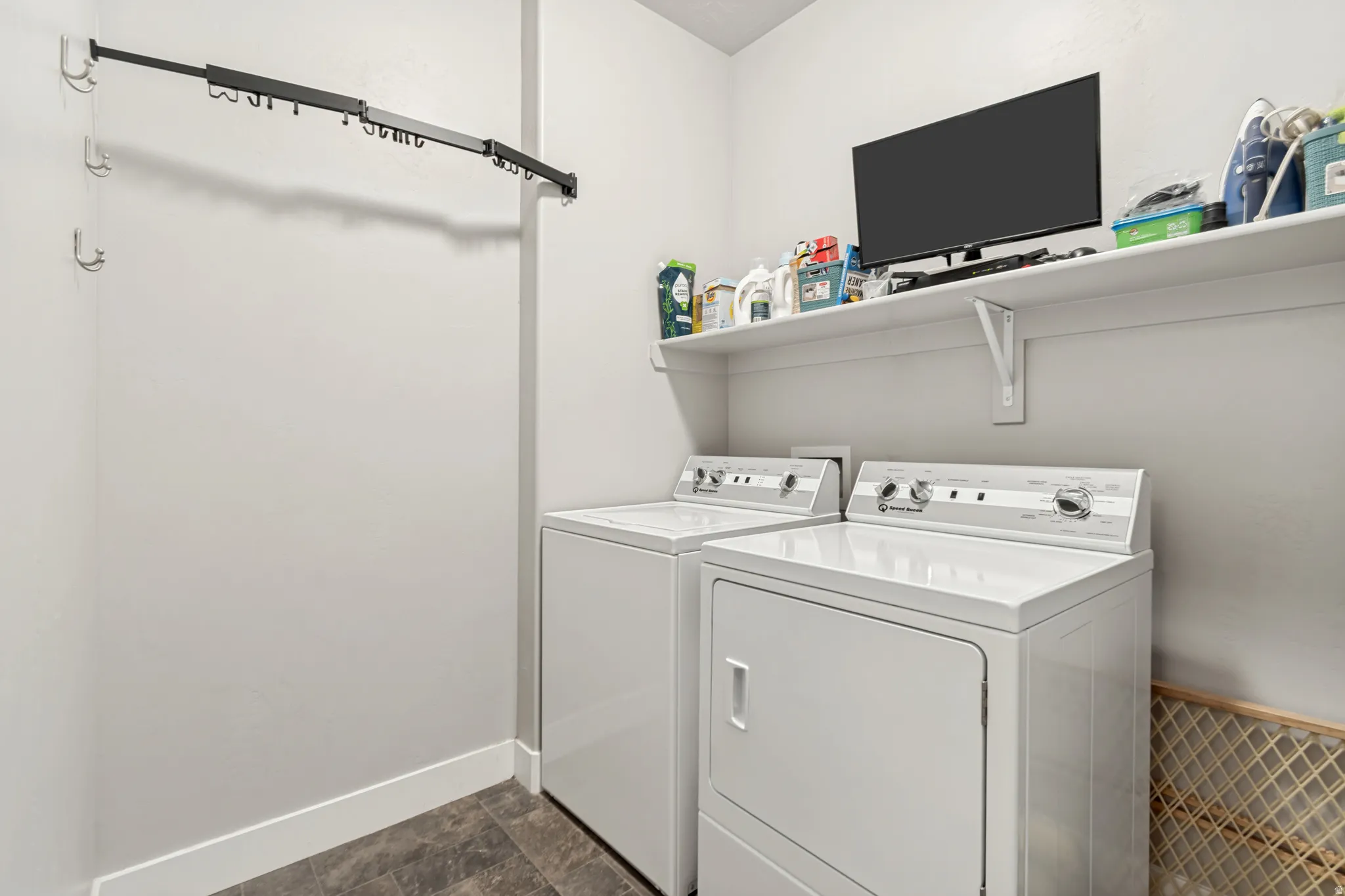 Dedicated laundry area featuring a full-size washer and dryer, integrated wall shelving, a wall-mounted television, and durable tile flooring