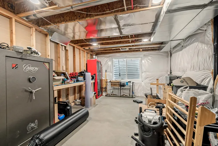 Unfinished basement space featuring exposed wooden joists, concrete flooring, perimeter insulation, a built-in workbench, and an egress window