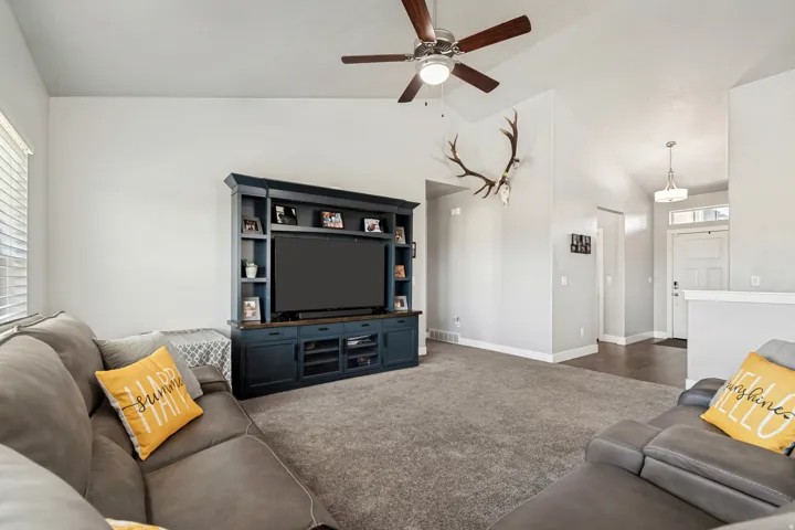 Spacious living area featuring vaulted ceilings, a ceiling fan with integrated lighting, and plush carpeting