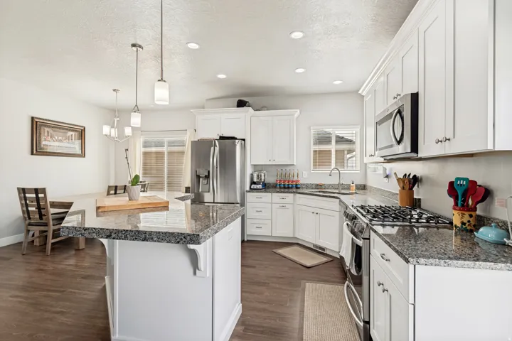 Kitchen featuring white cabinetry, stainless steel appliances, granite countertops, a center island with pendant lighting, and wood-finish flooring