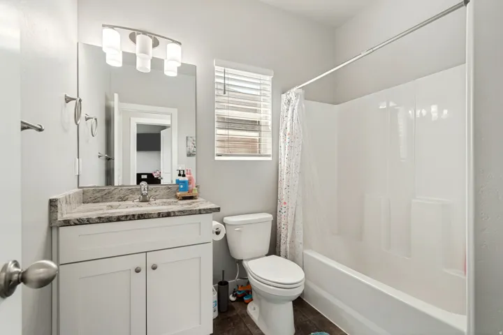 Bathroom featuring a white vanity with slab cabinet doors, a speckled countertop, and a rectangular mirror