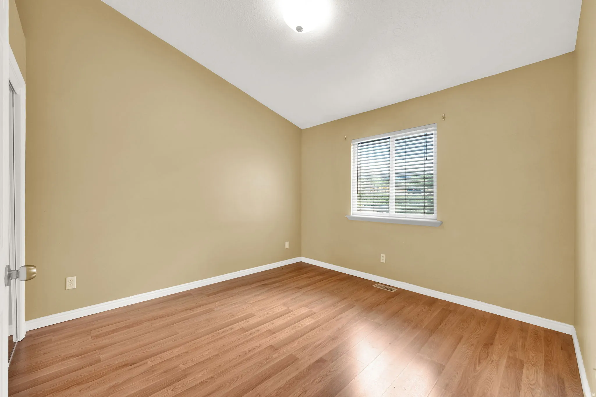 Room featuring wood-finish flooring, a vaulted ceiling, a window with blinds, and white trim