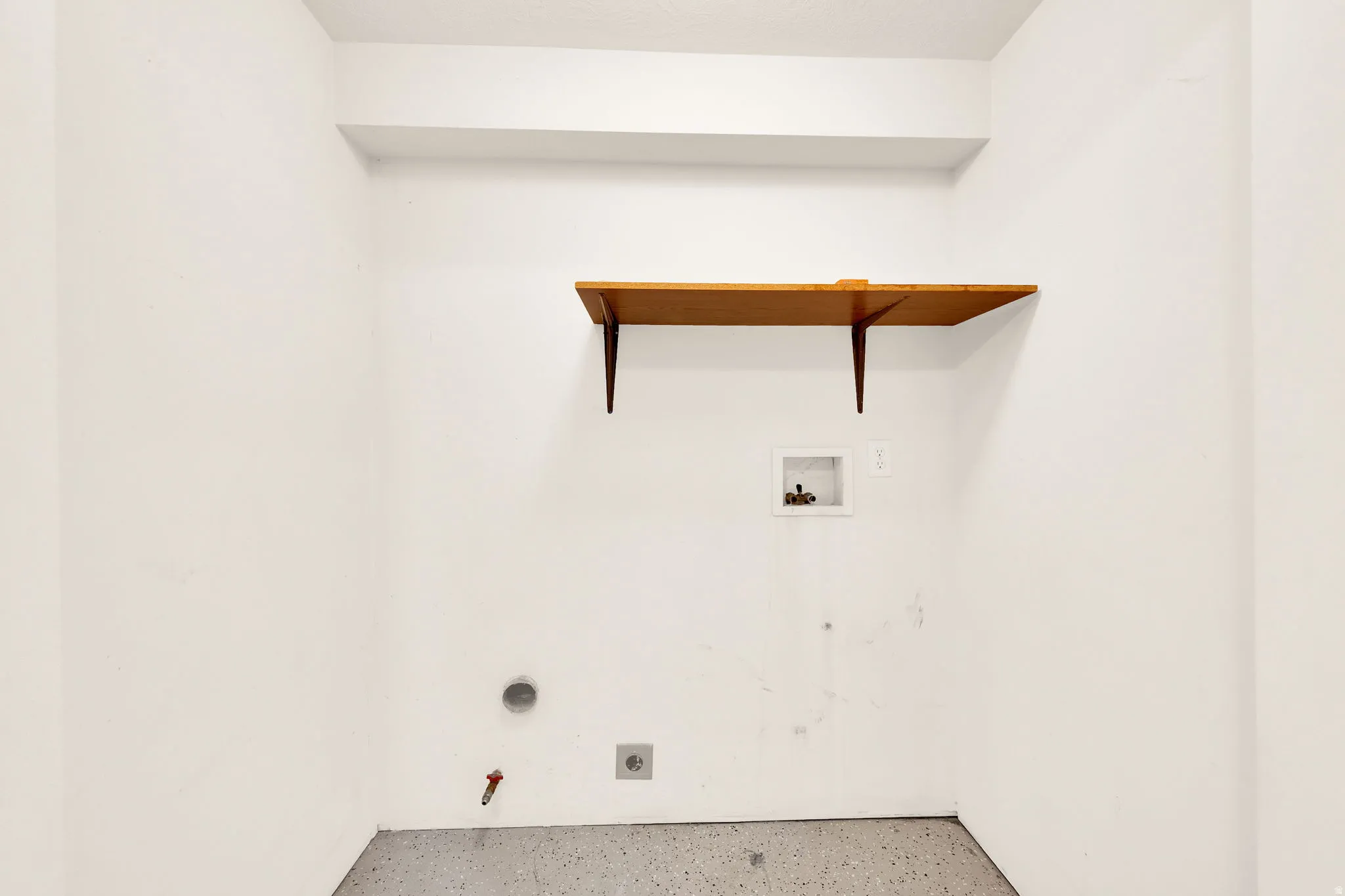 Dedicated utility space featuring a wood-finish wall shelf, white wall finishes, and a gray speckled floor