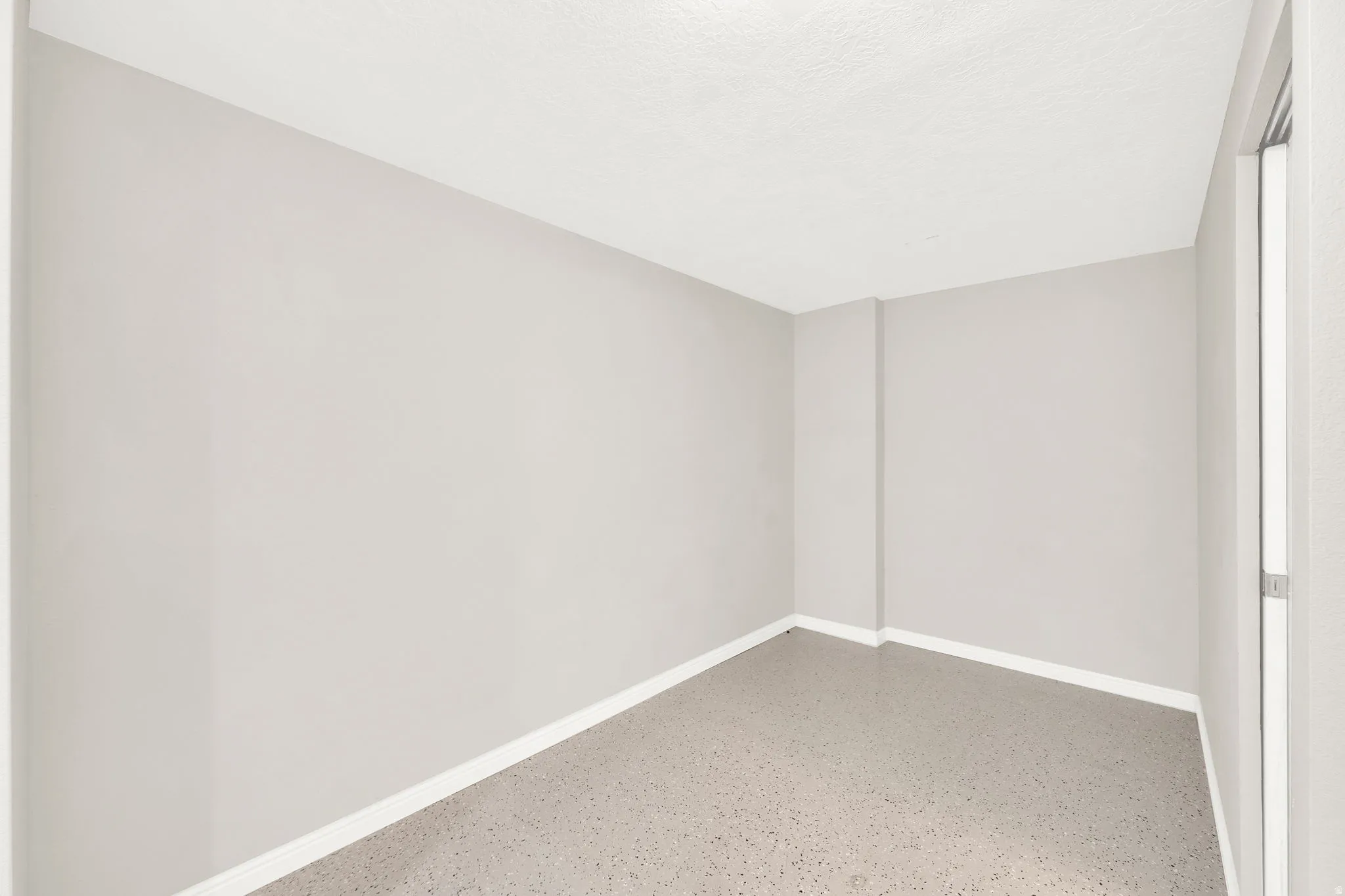 Room with light gray walls, white baseboards, and speckled gray flooring