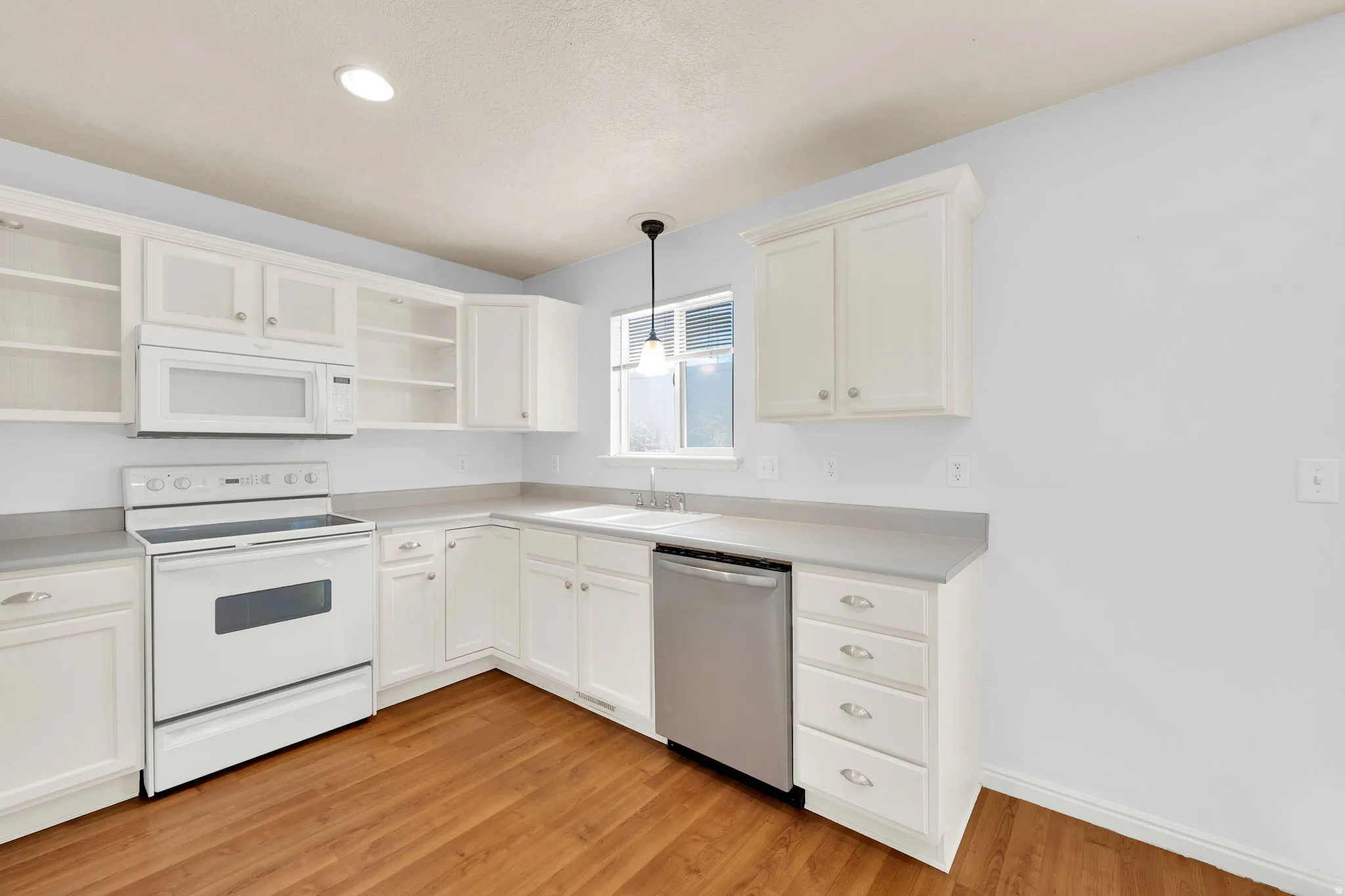 Kitchen featuring white cabinetry, light countertops, wood-finish flooring, stainless steel dishwasher, and white range with microwave