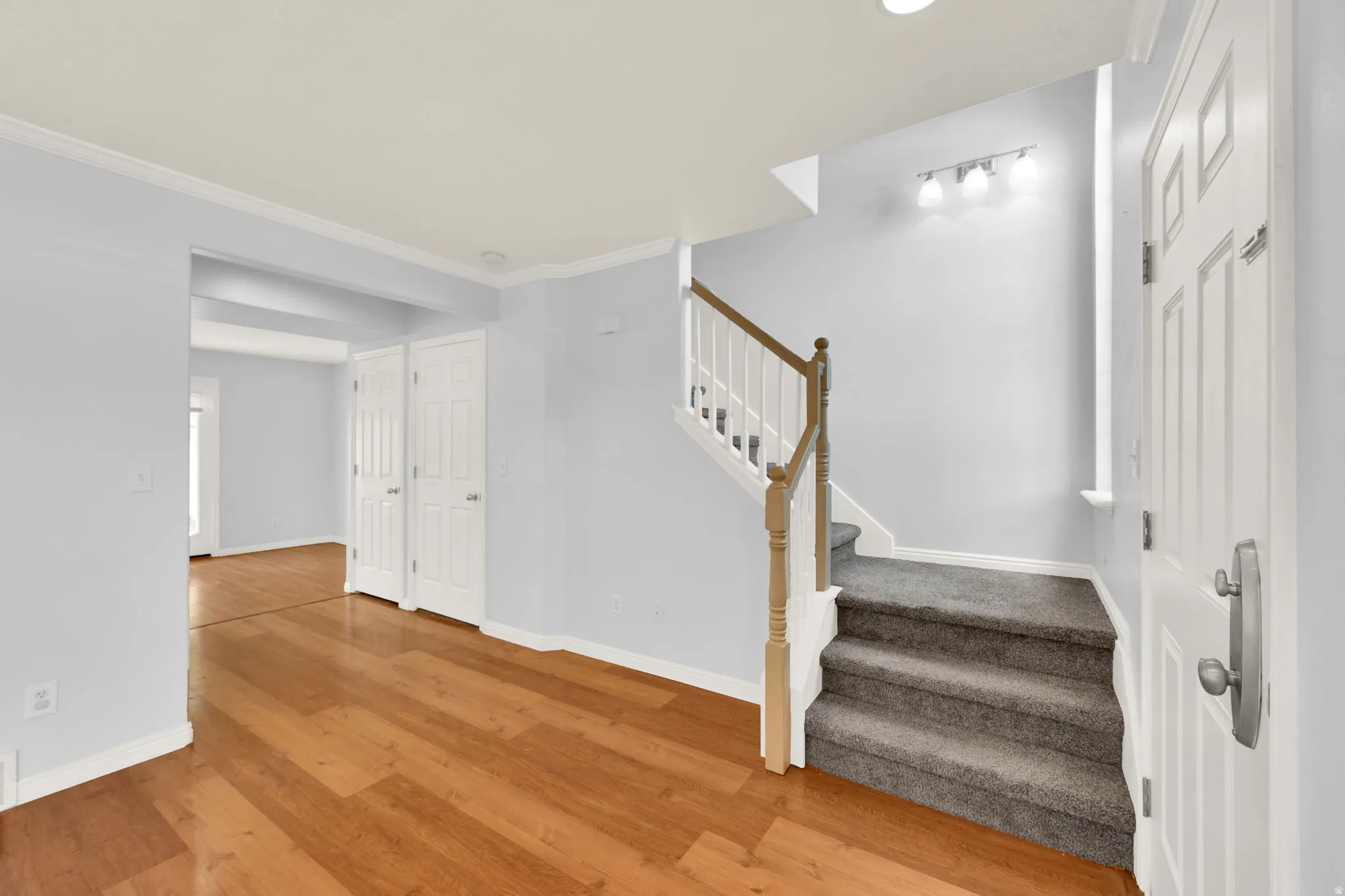 Foyer featuring wood-finish flooring, light grey wall paint, white trim, and a carpeted staircase with a wood handrail