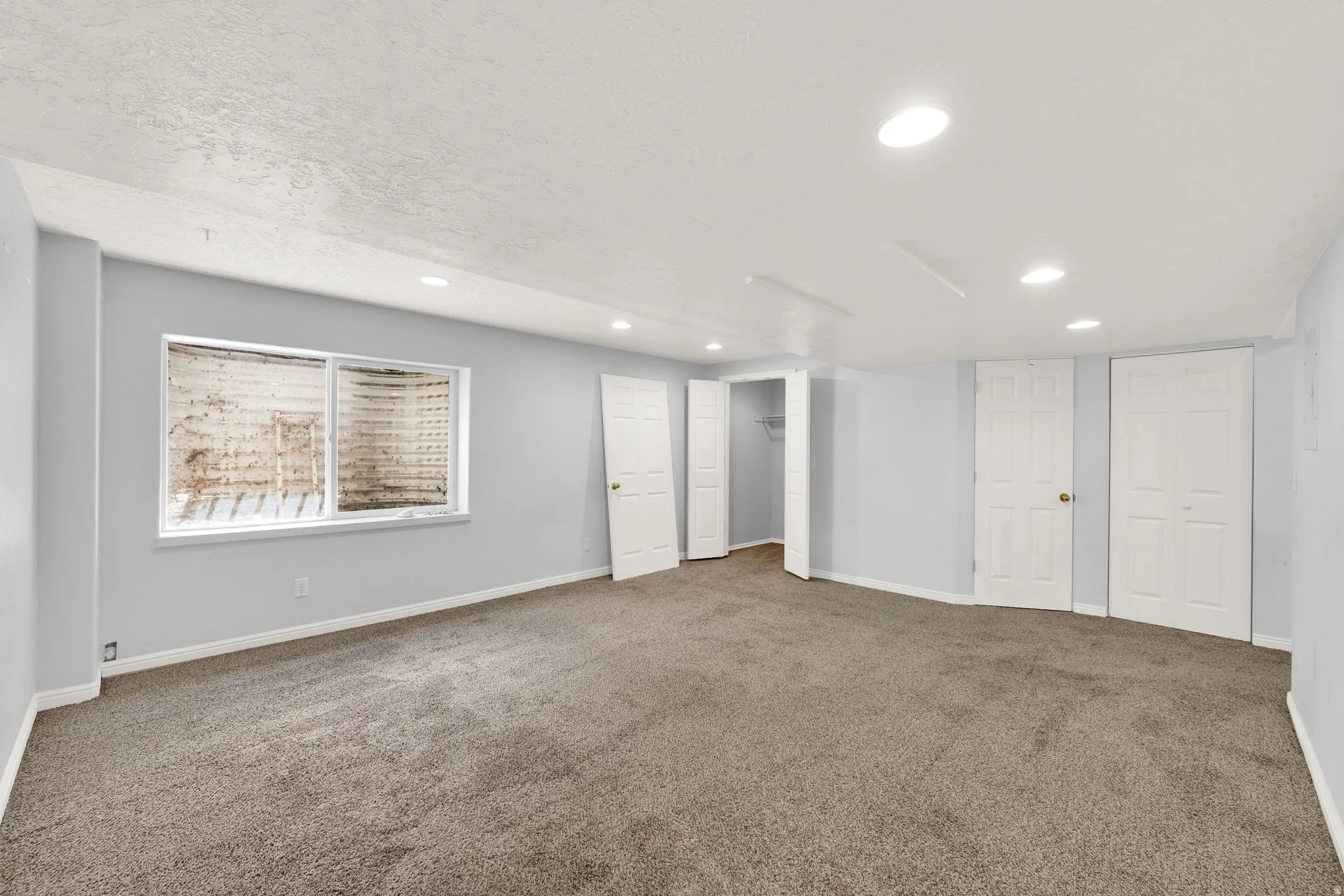 Spacious room with gray carpeting, light gray wall paint, and recessed ceiling lighting