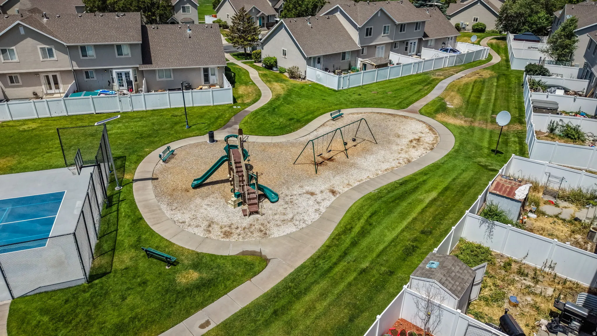 Central green space featuring a playground with swings and a slide structure, a basketball court, and paved walking paths