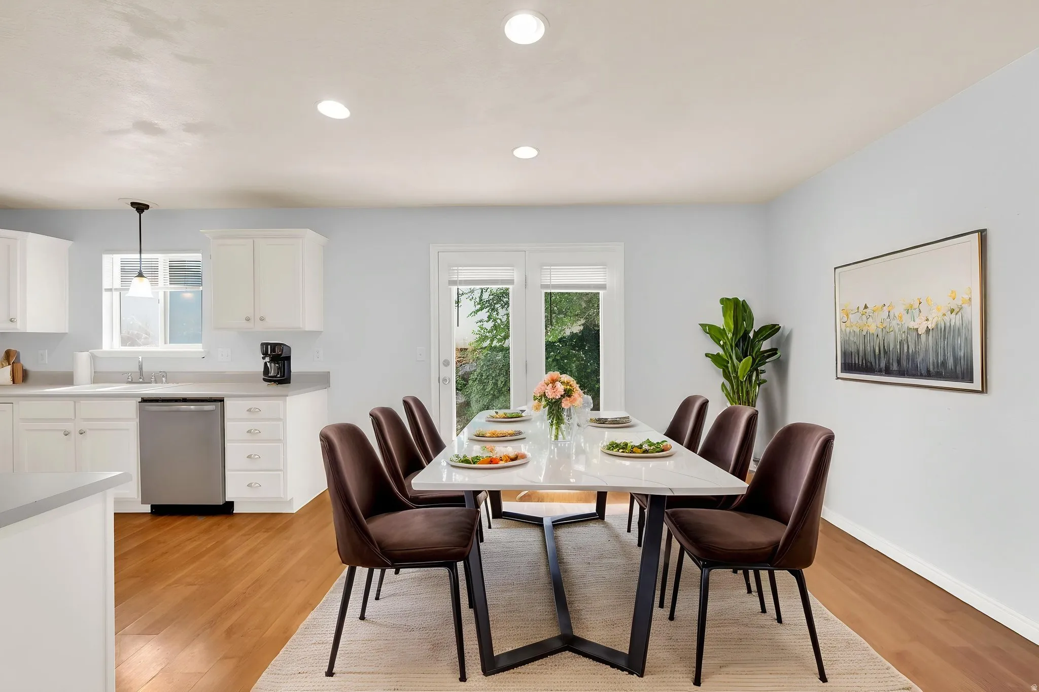 Open-concept dining area featuring a rectangular table with a white top and black base, wood-finish flooring, recessed lighting, and a double glass door