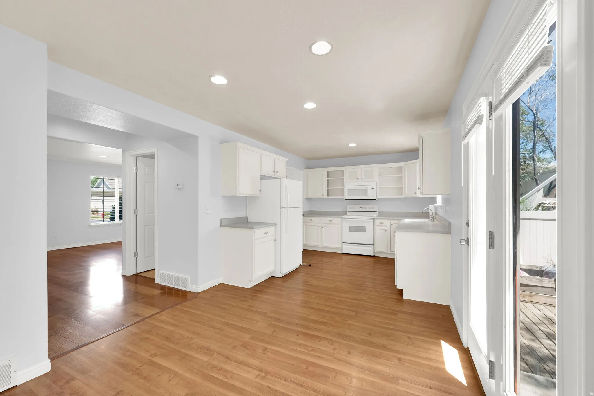 Open-concept kitchen and dining area featuring wood-finish flooring, white cabinetry, light-colored countertops, recessed lighting, and direct patio access through double glass doors