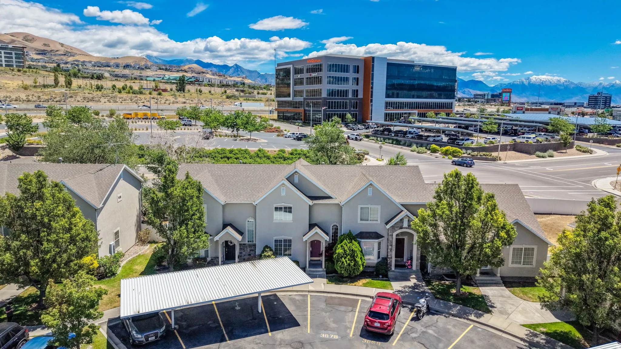 Gray stucco townhome complex with gabled roofs, stone accents, and carport parking