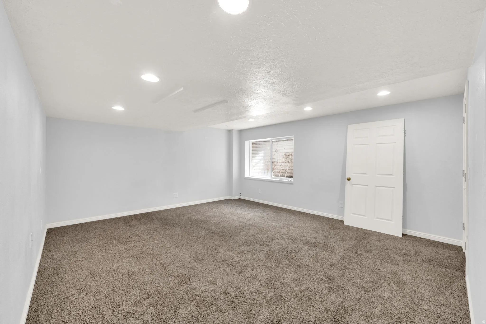 Spacious room featuring neutral carpeting, light-toned walls, and recessed lighting