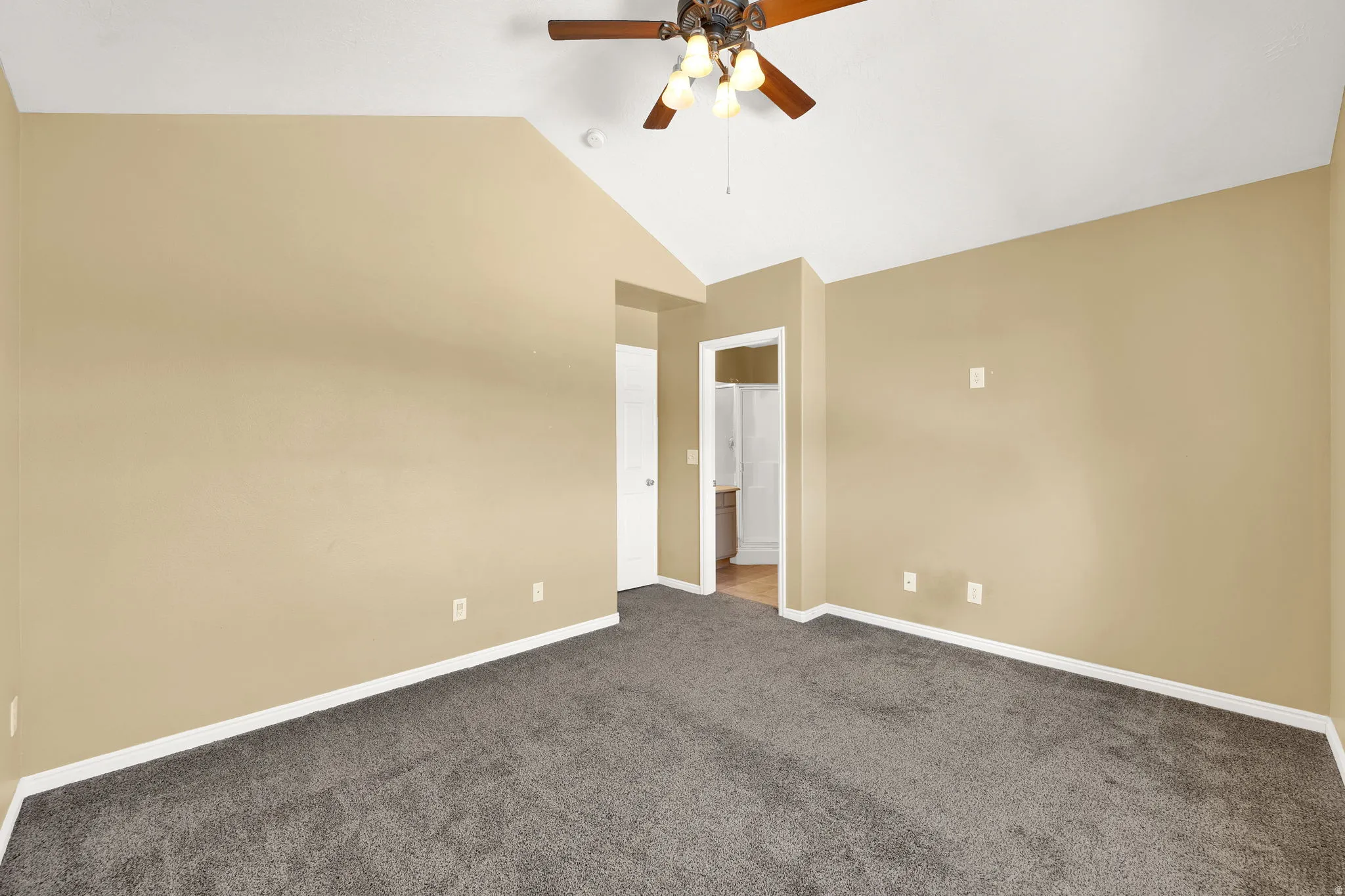 Carpeted room with vaulted ceiling and a ceiling fan with light fixture