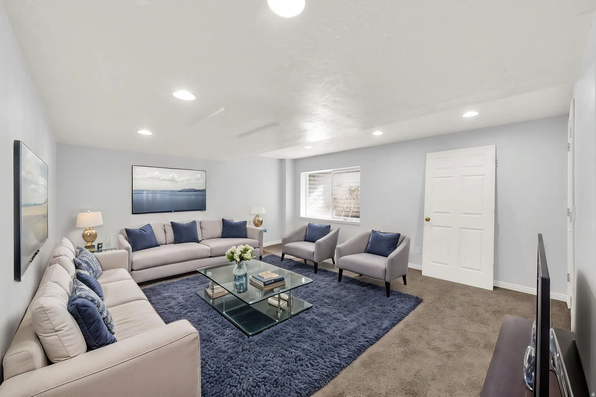 Spacious living area featuring light-colored walls, recessed lighting, and a window with a security grate