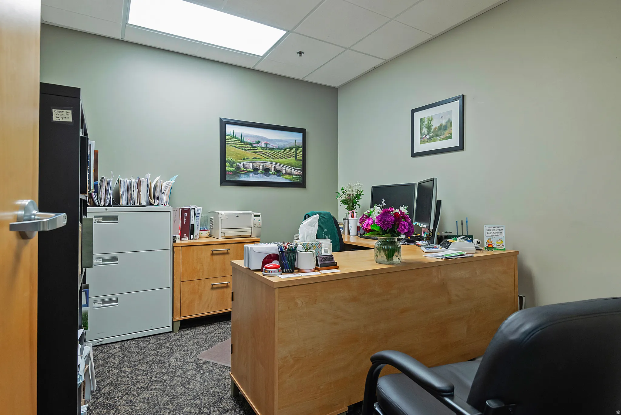 Office space featuring light green walls, a drop ceiling with integrated lighting, and patterned carpet flooring