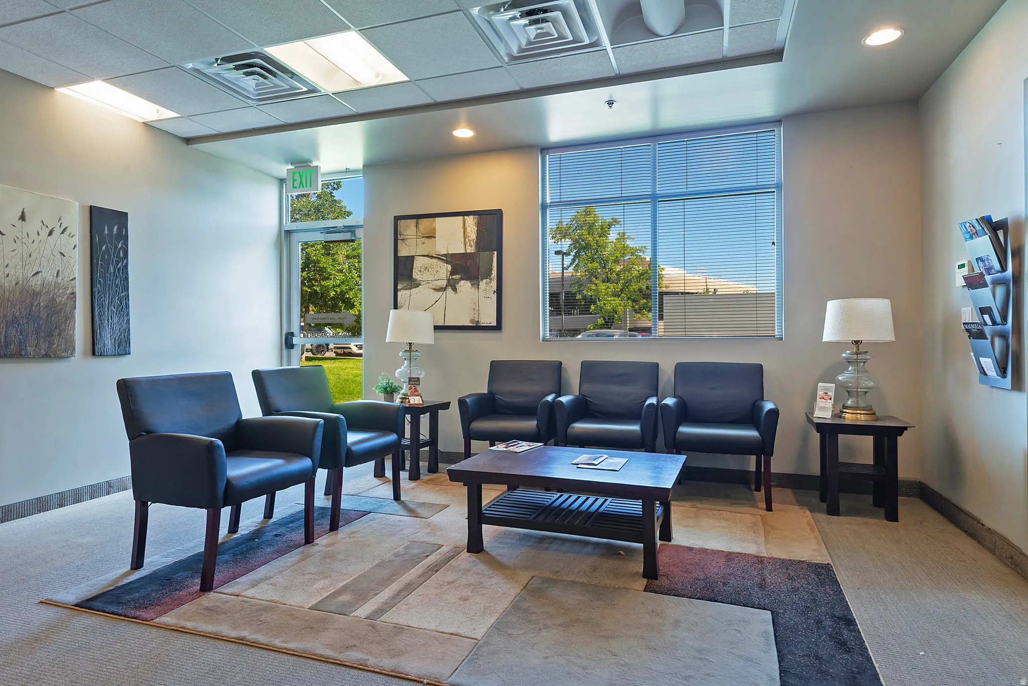 Spacious reception area featuring a full-glass entry door, large window with horizontal blinds, neutral wall tones, and recessed ceiling lighting