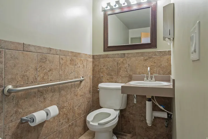 Bathroom featuring a wall-mounted sink, a framed mirror with overhead vanity lighting, and a toilet