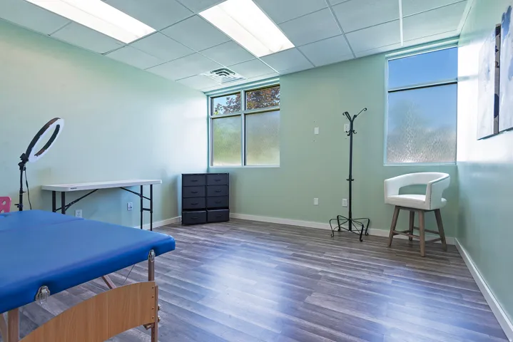 Spacious room featuring wood-finish flooring, two large windows, drop ceiling with recessed lighting, and light green wall paint
