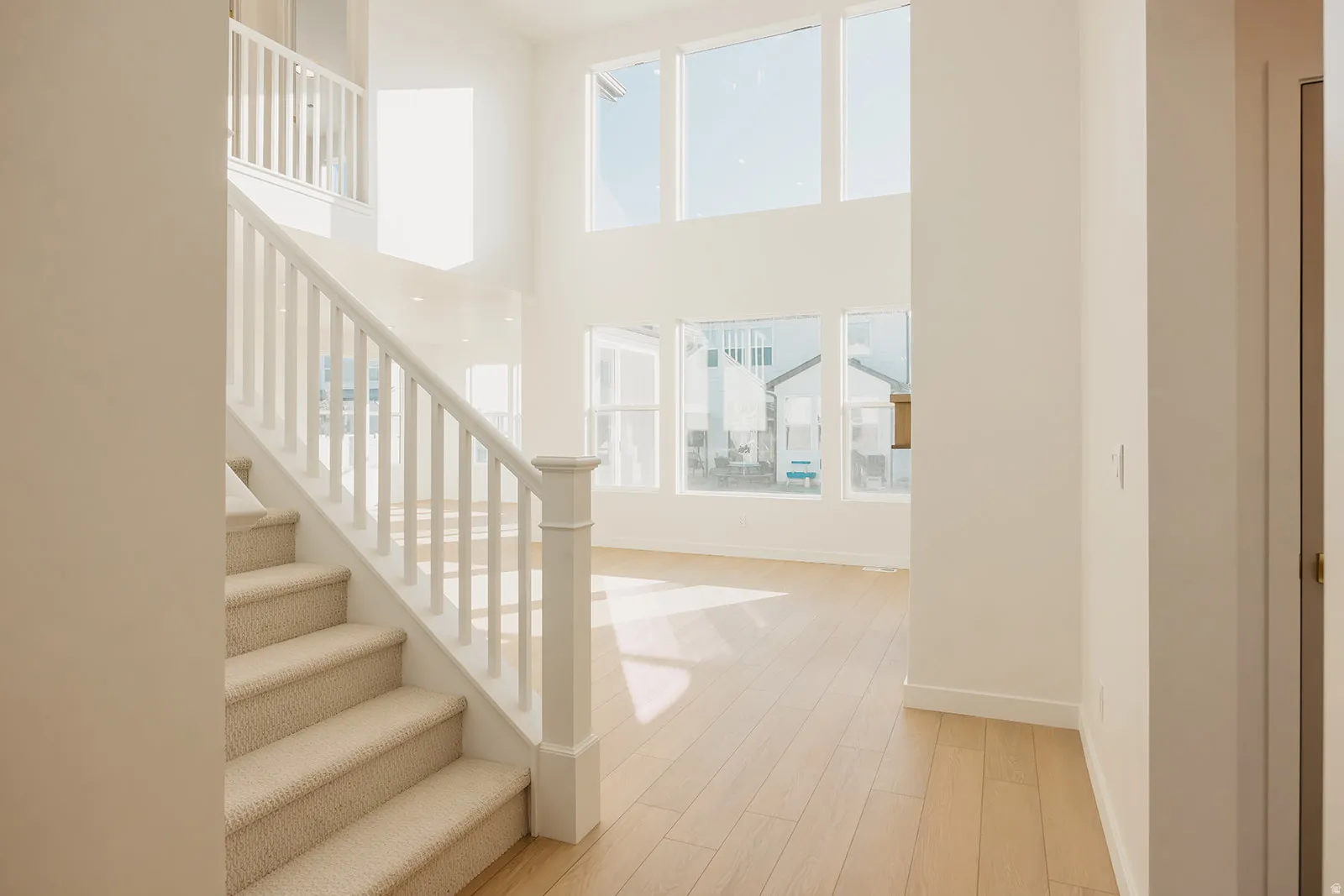 Carpeted staircase with white balusters, wood-finish flooring, and a two-story window array
