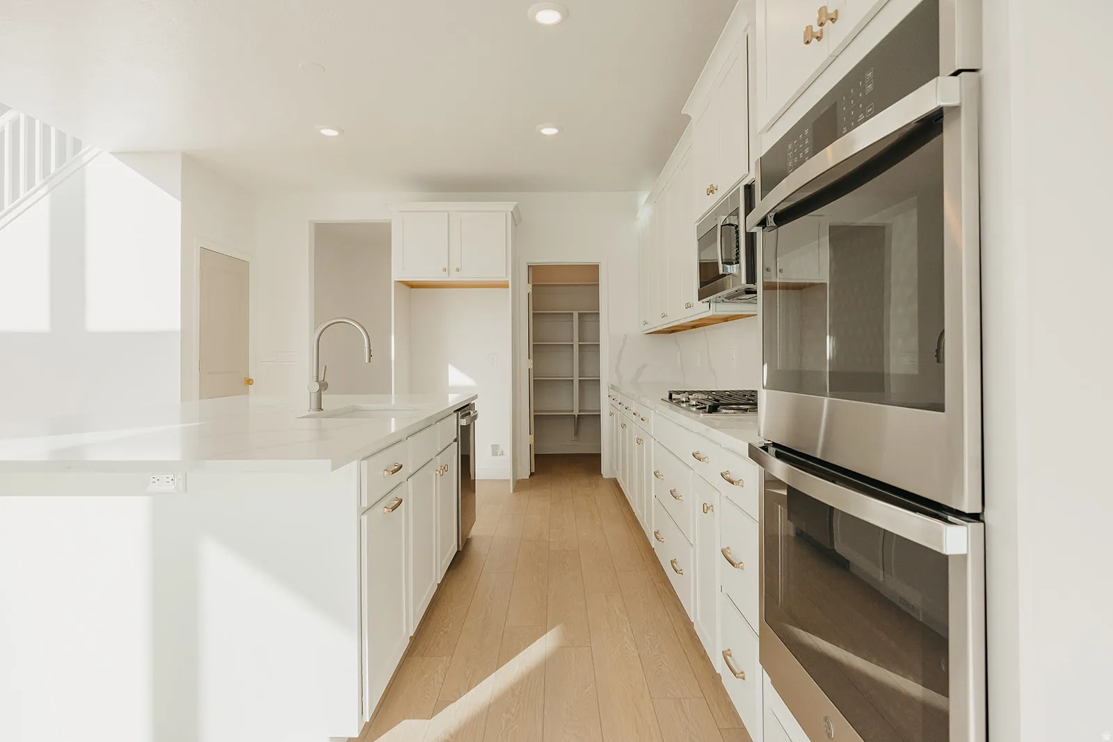 Kitchen featuring a large island with sink, white shaker cabinetry with gold-tone hardware, stainless steel appliances, and wood-finish flooring