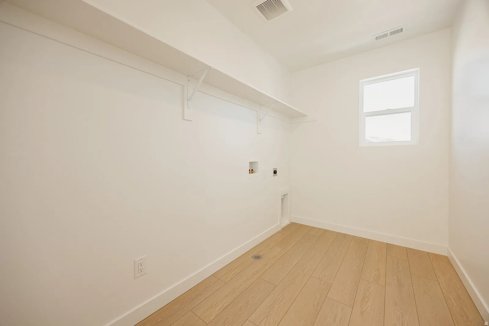 Laundry room featuring light wood-finish flooring, a white window, and built-in shelving