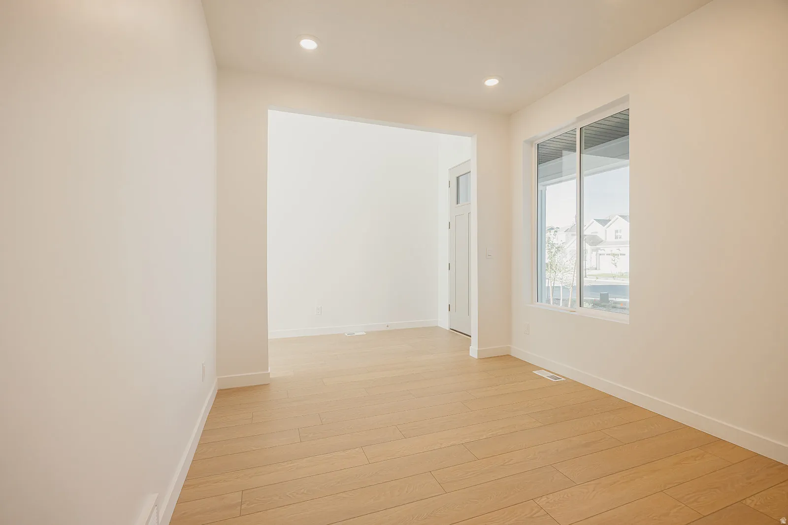 Open-concept office featuring light wood-finish flooring, recessed lighting, white baseboards, and a large window providing natural light