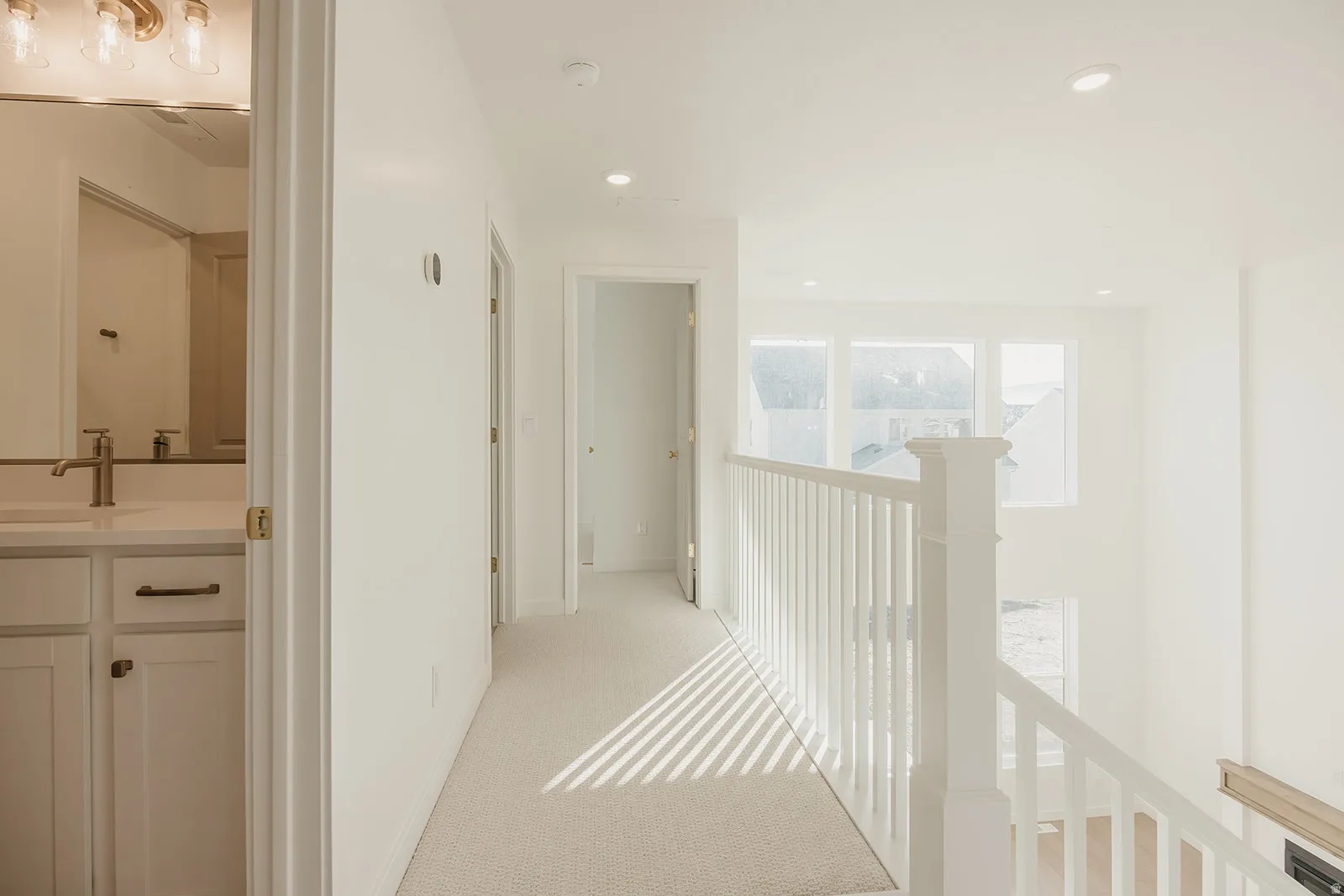 Upper-level hallway with neutral carpet, recessed lighting, and a white baluster railing