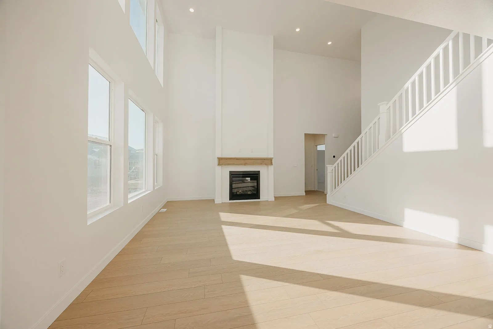 Vaulted ceilings highlight this expansive living area featuring a fireplace with a wood-finish mantel, abundant natural light from multiple windows, and light wood-finish flooring