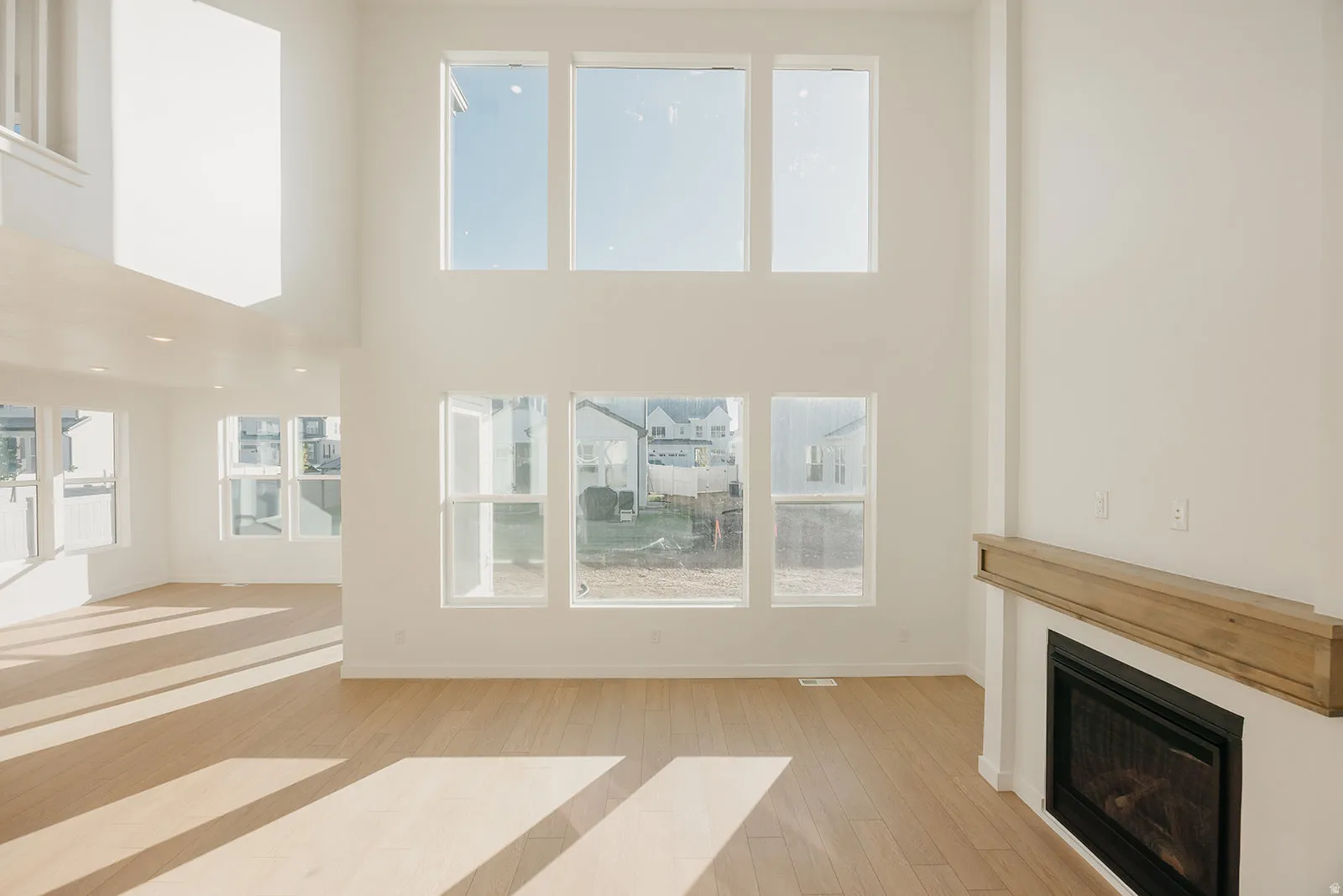 Two-story living area featuring a fireplace with a wood-finish mantel, wood-finish flooring, and multiple large windows