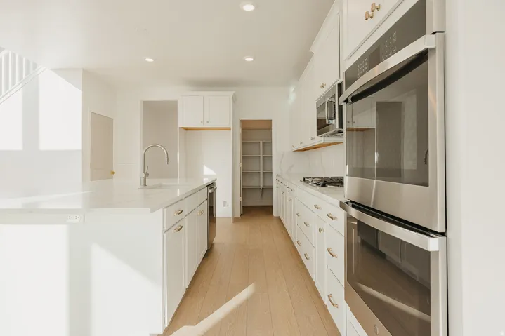 Kitchen featuring a large island with sink, white shaker cabinetry with gold-tone hardware, stainless steel appliances, and wood-finish flooring