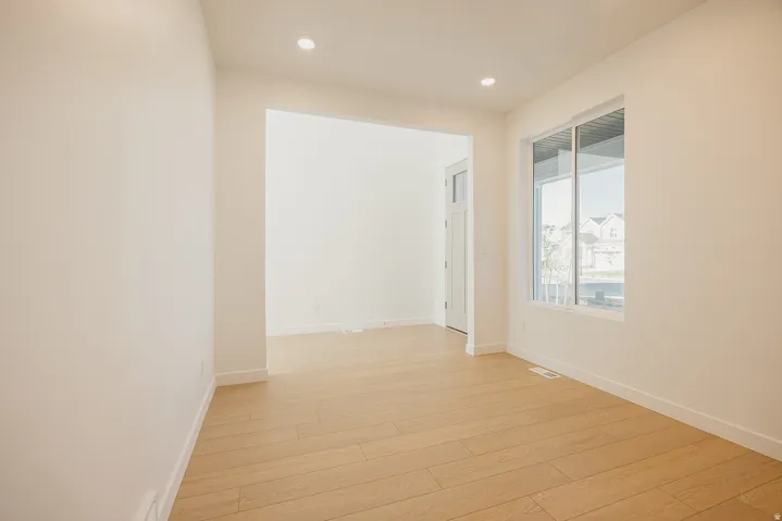 Open-concept office featuring light wood-finish flooring, recessed lighting, white baseboards, and a large window providing natural light