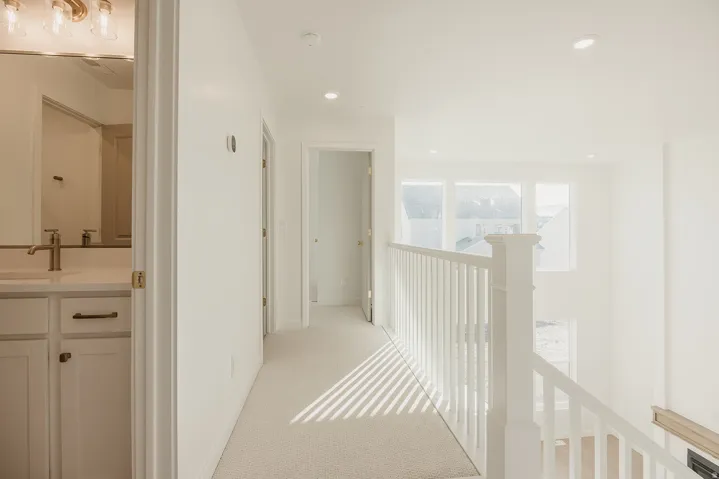 Upper-level hallway with neutral carpet, recessed lighting, and a white baluster railing