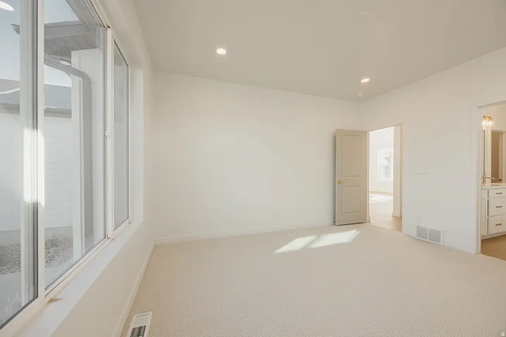 Spacious room featuring light neutral carpeting, recessed ceiling lighting, a large window providing ample natural illumination, and crisp white walls
