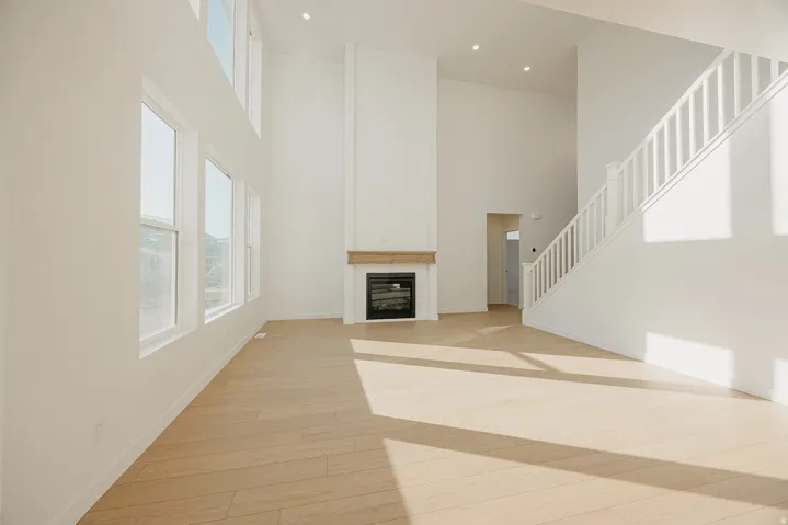 Vaulted ceilings highlight this expansive living area featuring a fireplace with a wood-finish mantel, abundant natural light from multiple windows, and light wood-finish flooring