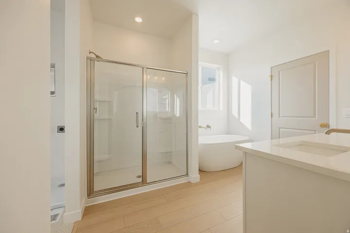 Primary bathroom featuring a glass-enclosed shower, freestanding soaking tub, single vanity with integrated sink, wood-finish flooring, and recessed lighting