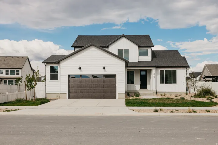 Farmhouse style two-story residence featuring white siding, a dark roof, and a two-car garage with a textured brown door