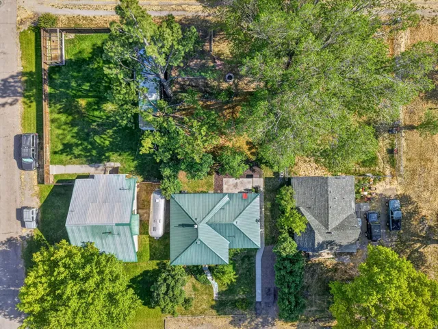 Aerial property overview showcasing a residential structure with a green metal roof, a paved walkway, and surrounding green spaces