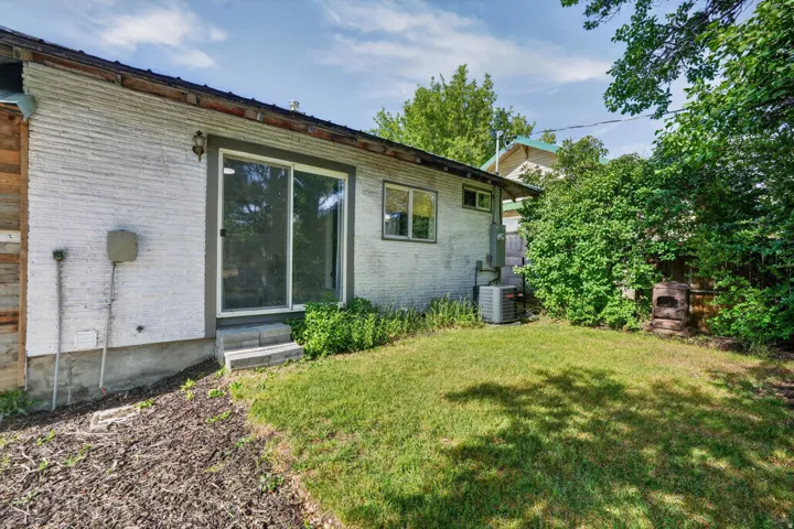 Rear exterior featuring a sliding glass door, white brick facade, and a grass lawn