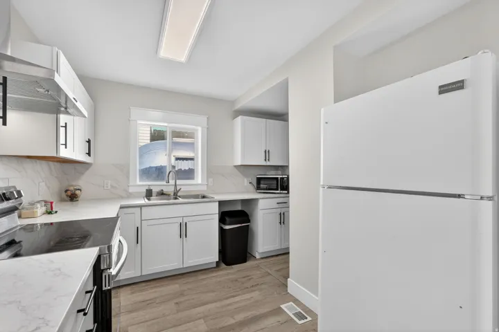 Bright kitchen featuring white cabinetry with black hardware, white countertops, wood-finish flooring, and a stainless steel range with overhead ventilation