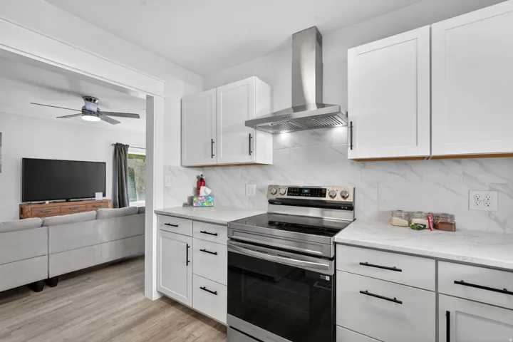Modern kitchen featuring white shaker cabinetry with black hardware, stainless steel appliances, a range hood, and light-toned countertops