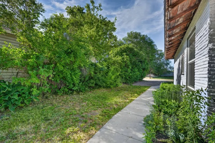 Side yard featuring a concrete walkway, mature trees, and established shrubbery