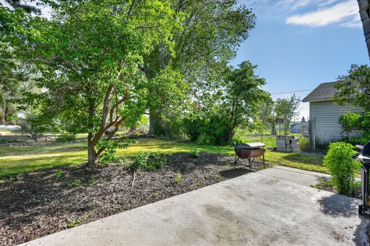 Concrete patio area featuring a mulched planting bed, mature trees, and a grassy expanse