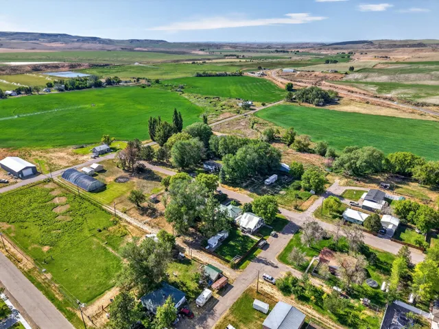 Expansive rural landscape featuring vibrant green fields, multiple structures including a large agricultural building and a greenhouse, and a small body of water
