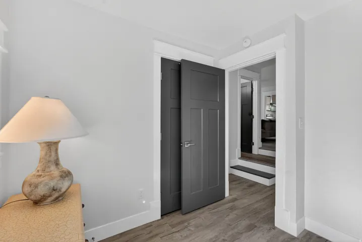 Interior room featuring light gray walls, wood-finish flooring, white baseboards, and a dark gray paneled door with brushed nickel hardware
