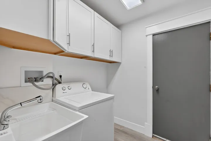 Utility room featuring white cabinetry with silver hardware, a utility sink with a chrome faucet, and wood-finish flooring