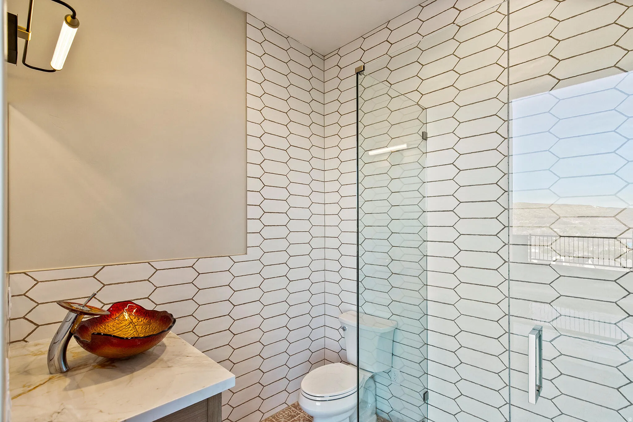 Modern bathroom featuring an enclosed shower with a clear glass door, white elongated hexagonal tile walls, and a light-colored vanity with a vessel sink