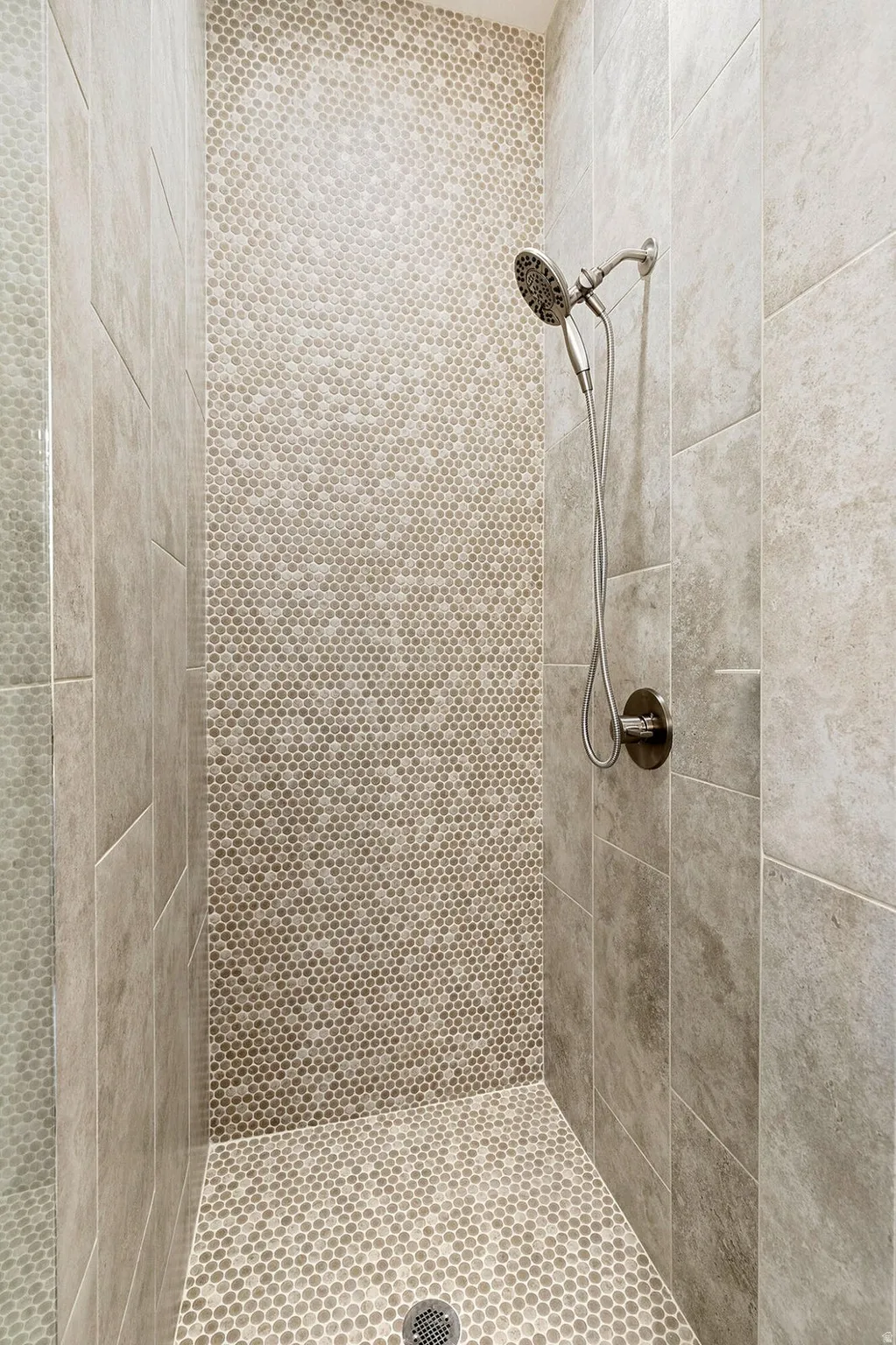 Shower enclosure featuring large format wall tiles, penny tile accent wall, penny tile shower floor, and a brushed nickel shower head with handheld attachment